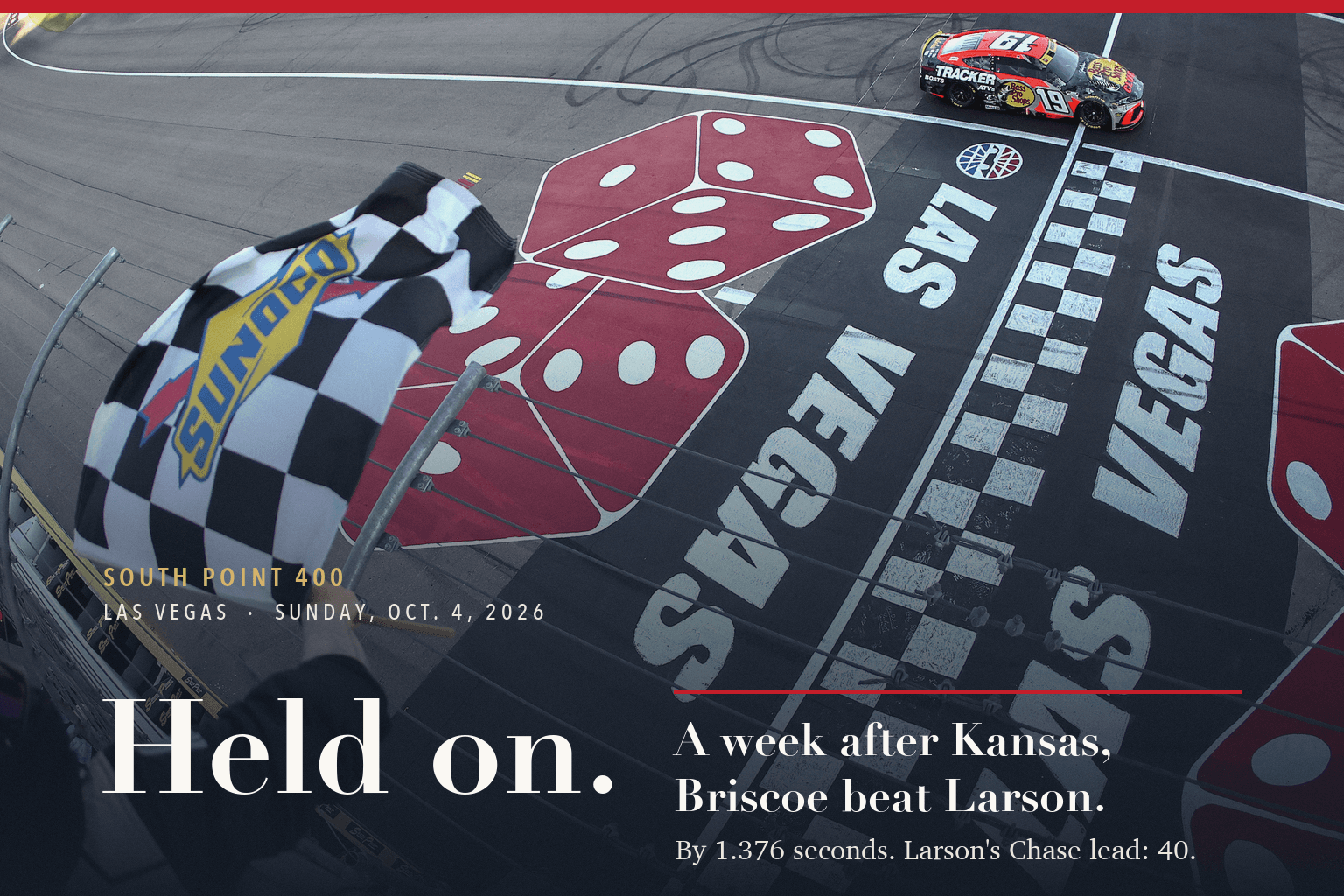 Chase Briscoe's No. 19 Toyota takes the checkered flag at Las Vegas Motor Speedway, seen from above, as a flagman waves it beside the dice painted on the track.